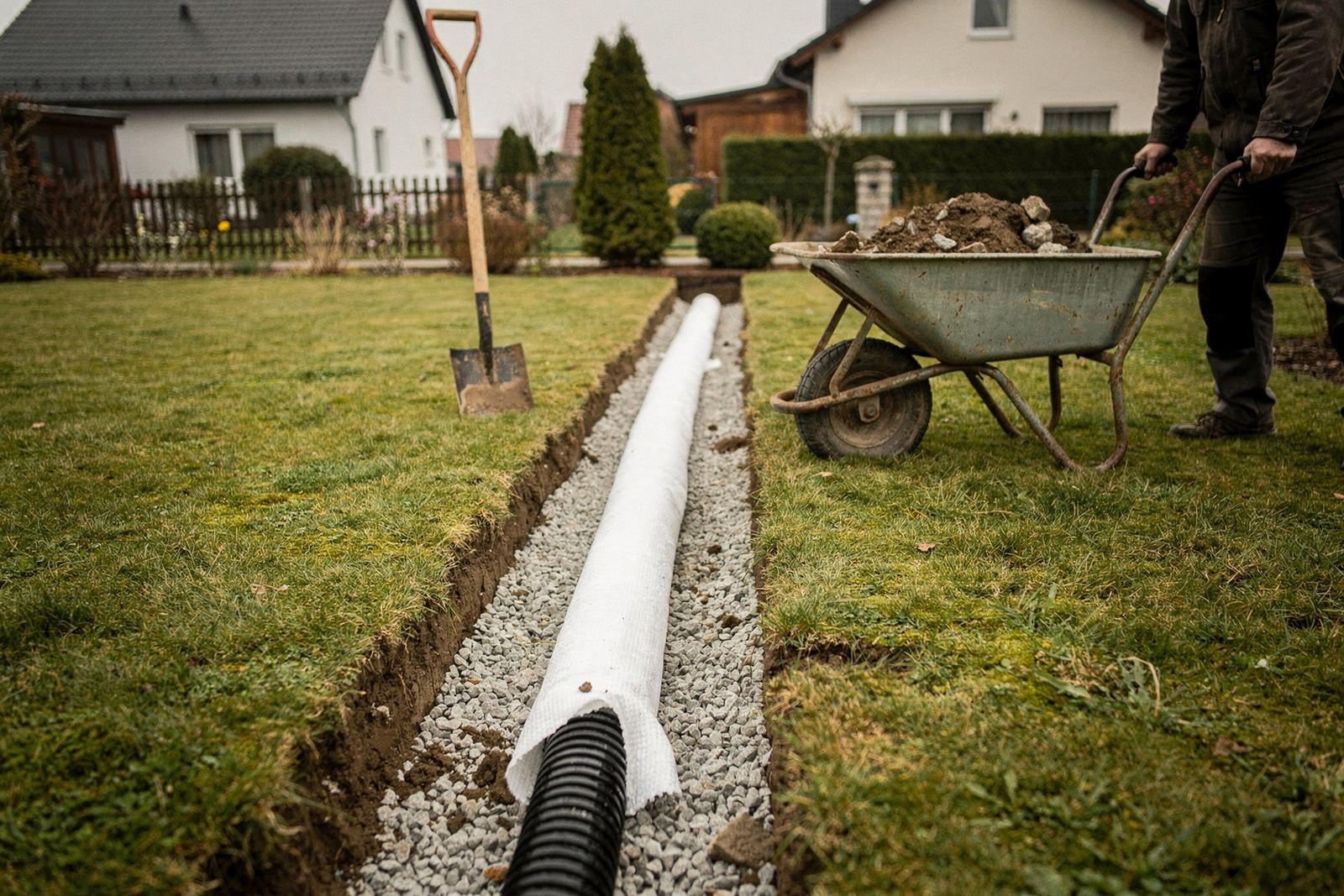 Symbolbild: Offener Graben im Garten mit Drainagerohr auf Kies und Filtervlies