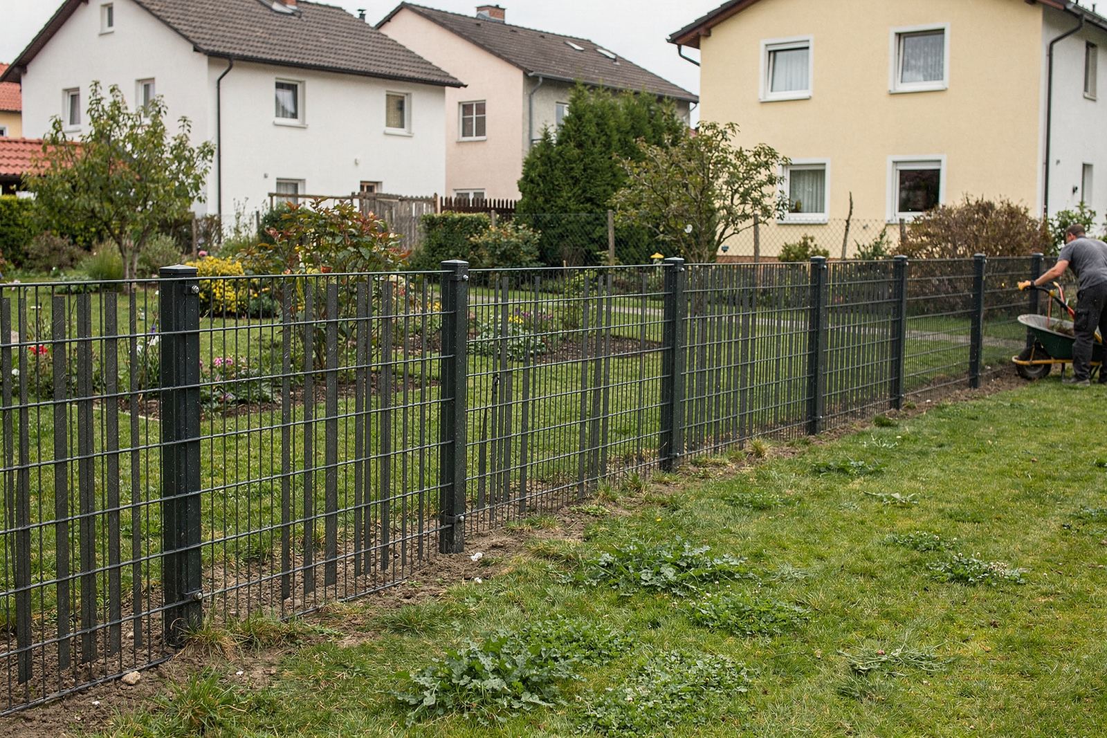 Symbolbild: Doppelstabmattenzaun in Anthrazit an einer Rasenfläche, daneben Sichtschutzelemente aus Holz